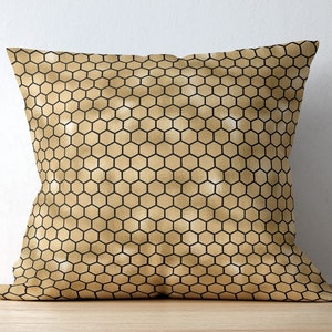 May include: A square throw pillow featuring a metallic gold finish with a repeating black honeycomb pattern. The surface has a subtle sheen and a consistent geometric grid of hexagons covering the entire front face of the pillow cover.