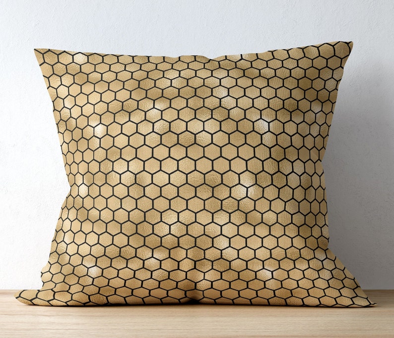 May include: A square throw pillow featuring a metallic gold finish with a repeating black honeycomb pattern. The surface has a subtle sheen and a consistent geometric grid of hexagons covering the entire front face of the pillow cover.