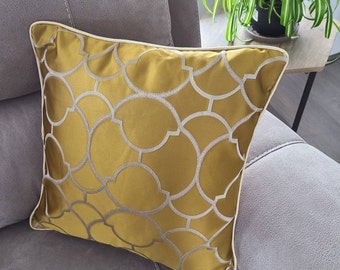 May include: A mustard yellow cushion with a white geometric pattern. The cushion is on a grey sofa.