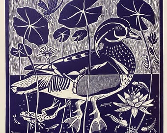 May include: A wood duck with a white and black patterned body is swimming in a pond with lily pads and a frog. The image is a blue and white woodblock print with the text "Wood Duck on Rosemary" and "V. Frey Jackson 2021" at the bottom.