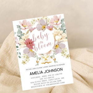 May include: A floral baby shower invitation with a pink and white floral design. The text reads "baby in bloom" and includes the name Amelia Johnson, the date and time of the shower, the location, and RSVP information.