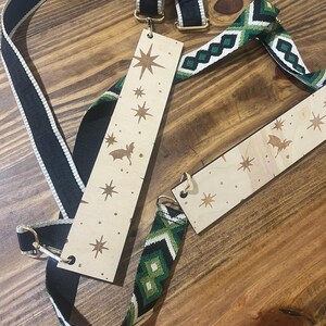 May include: A collection of bag straps and wooden tags on a wooden surface. One strap is black with a white stripe, and another is green and white with a geometric pattern. The wooden tags have star and bat designs.