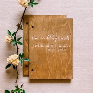 May include: A wooden box with a light brown stain. The box has two holes on the left side and is engraved with the text "Our wedding cards William & Jennifer 02.21.2020".