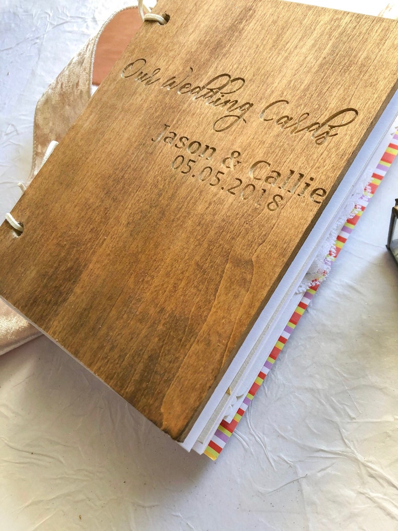 May include: A wooden guest book with the text "Our Wedding Calender" and "Jason & Callie 05.05.2018" engraved on the cover.