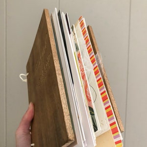 May include: A wooden-cover journal with a variety of colorful patterned pages. The journal is bound with a white string and has a natural wood finish.