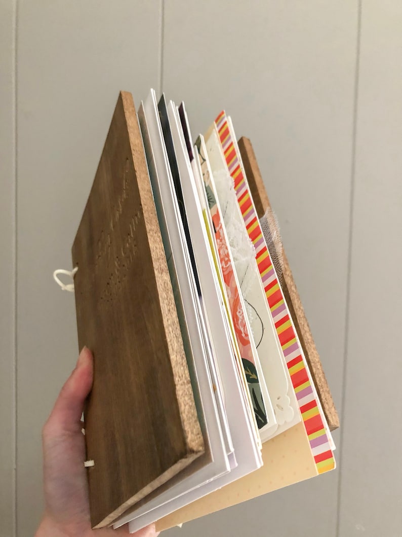 May include: A wooden-cover journal with a variety of colorful patterned pages. The journal is bound with a white string and has a natural wood finish.