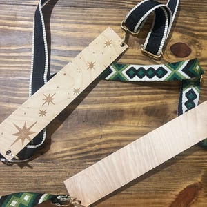 May include: Wooden bag strap with starburst and star designs, paired with a black and white striped strap and a green and white patterned strap. The straps have gold-colored metal hardware and are displayed on a wooden surface.