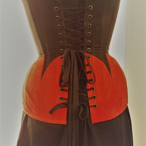 May include: A black and red corset with a lace-up back. The corset has a pointed shape at the bottom and is made of a sturdy fabric.