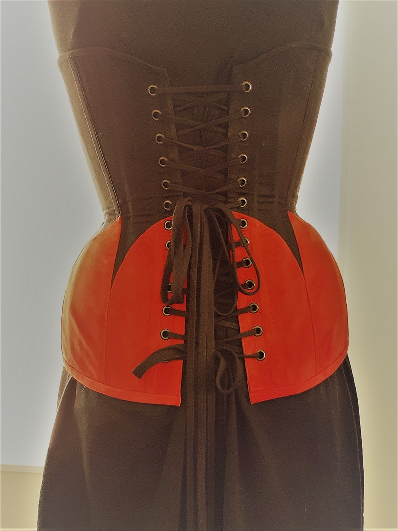 May include: A black and red corset with a lace-up back. The corset has a pointed shape at the bottom and is made of a sturdy fabric.