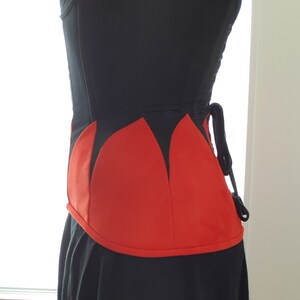 May include: A black corset with a red, pointed, petal-shaped design at the bottom. The corset has a lace-up back.