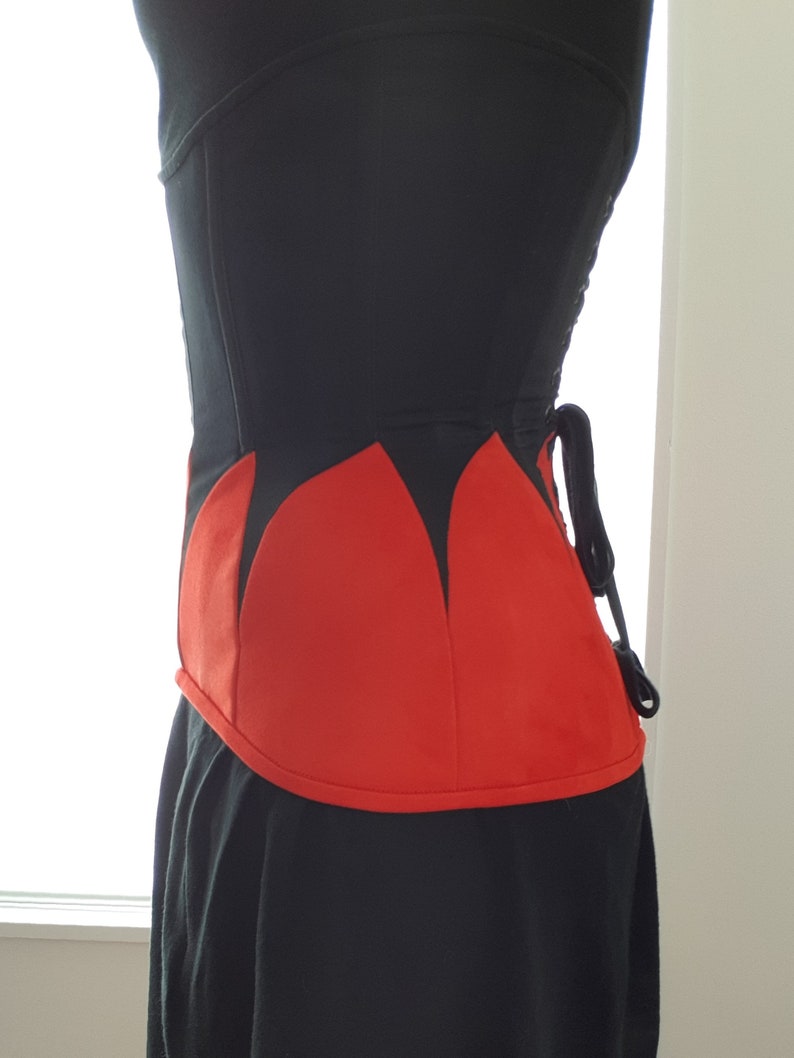 May include: A black corset with a red, pointed, petal-shaped design at the bottom. The corset has a lace-up back.