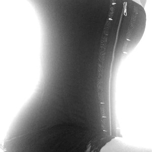 Puede incluir: Un cors&eacute; negro sin tirantes con una cremallera en la parte delantera y tachuelas plateadas a lo largo de la cremallera. El cors&eacute; tiene un ribete de encaje en la parte inferior.