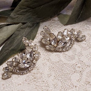 May include: A pair of silver tone earrings with clear crystal rhinestones arranged in a floral design.