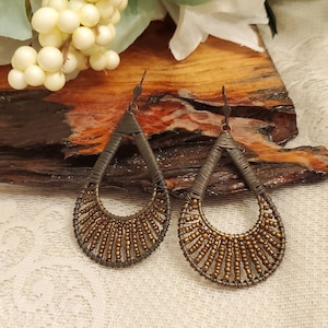 May include: A pair of teardrop-shaped earrings made of wire wrapped with small gold beads. The earrings are a dark bronze color.