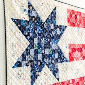 May include: A white, blue, and red patchwork quilt with a large blue star in the center. The star is made up of smaller squares of fabric in various shades of blue. The quilt is quilted with a diamond pattern.