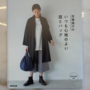 May include: A book cover featuring a woman wearing a black coat, white shirt, and gray pants, holding a blue bag. The book title is in Japanese, with the words "Clothes and Bags" and "Always Comfortable".