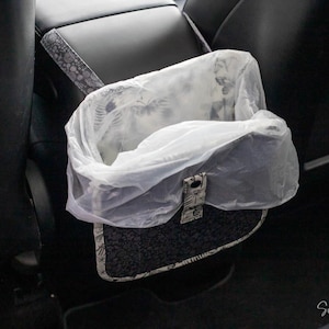 May include: A car trash bag with a patterned exterior and a clear plastic liner. The bag is designed to hang from the back of a car seat. The bag has a decorative clasp.
