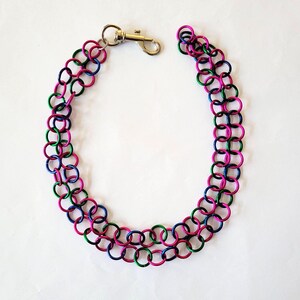 May include: A colorful chainmail necklace with a lobster clasp. The necklace is made of interlocking metal rings in pink, green, and blue. The chain is approximately 18 inches long.