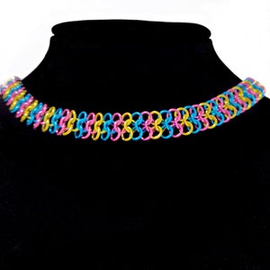 May include: A colorful chain necklace made of linked metal rings in pink, blue, and gold.