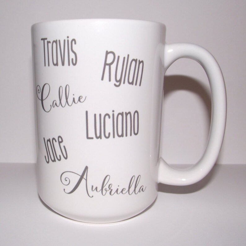 May include: White ceramic mug with a curved handle. The mug features the names "Travis", "Callie", "Jace", "Rylan", "Luciano", and "Aubriella" in grey lettering. The mug is a standard size for coffee or tea.