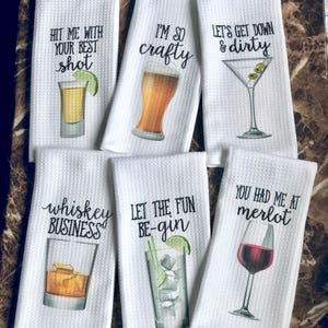 May include: Set of six white kitchen towels with humorous drink-themed sayings and illustrations. The towels feature phrases like "Hit me with your best shot", "I'm so crafty", "Let's get down & dirty", "Whiskey business", "Let the fun be-gin", and "You had me at merlot".