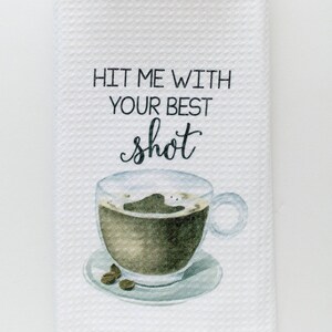 May include: White kitchen towel with the text "Hit me with your best shot" and a watercolor illustration of a cup of coffee with coffee beans.