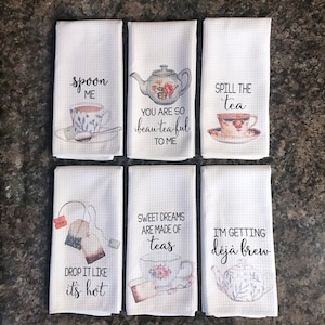 May include: Set of six white tea towels with tea-themed sayings and illustrations. The sayings include "Spoon Me", "You Are So Beautea-ful To Me", "Spill The Tea", "Drop It Like It's Hot", "Sweet Dreams Are Made Of Teas", and "I'm Getting Deja Brew".