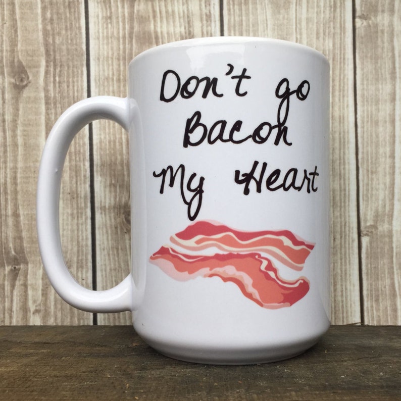 May include: White ceramic coffee mug with a black handwritten message that says "Don't go bacon my heart" and a cartoon image of a strip of bacon.