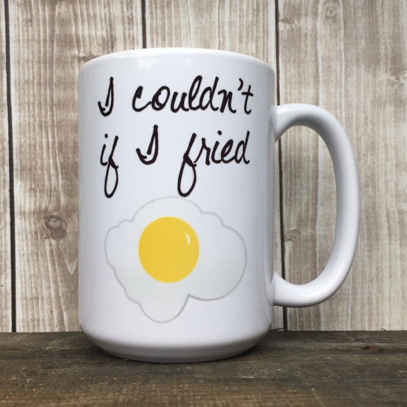 May include: White ceramic mug with a black handwritten saying "I couldn't if I tried" and a cartoon image of a fried egg.