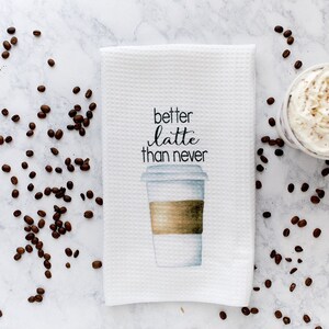 May include: White kitchen towel with a brown and white coffee cup illustration and the text "better latte than never".