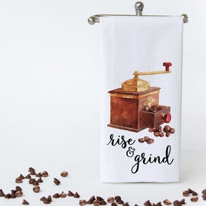 May include: White kitchen towel with a watercolor illustration of a vintage coffee grinder and coffee beans. The text "rise & grind" is printed in black below the illustration.