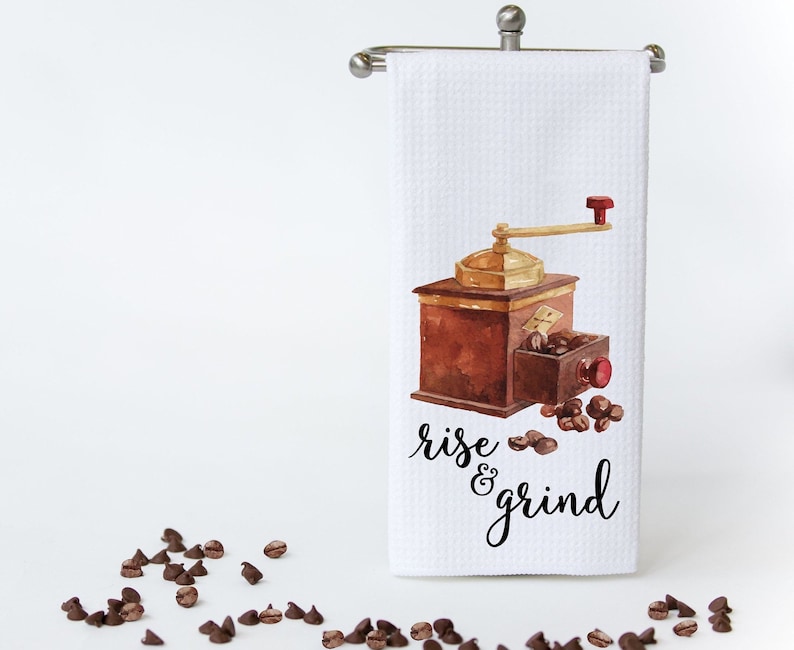 May include: White kitchen towel with a watercolor illustration of a vintage coffee grinder and coffee beans. The text "rise & grind" is printed in black below the illustration.