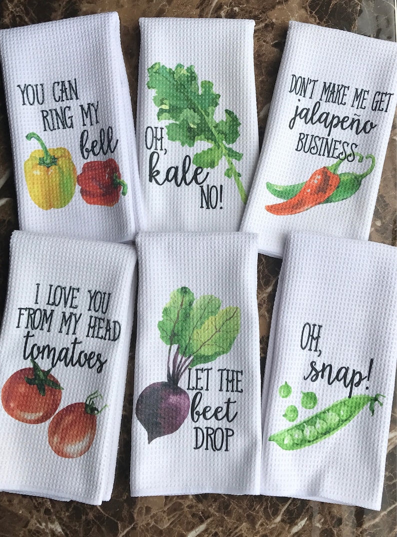 K&ouml;nnte beinhalten: Satz von sechs wei&szlig;en K&uuml;chent&uuml;chern mit bunten Gem&uuml;seillustrationen und humorvollen Spr&uuml;chen. Die Handt&uuml;cher zeigen eine Paprika, eine rote Paprika, Gr&uuml;nkohl, eine Jalape&ntilde;o-Paprika, Tomaten, eine Rote Bete und Erbsen. Die Spr&uuml;che lauten: "You can ring my bell", "Oh, kale no!", "Don't make me get jalapeno business", "I love you from my head tomatoes", "Let the beet drop" und "Oh, snap!"