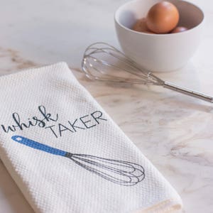 May include: White kitchen towel with blue text that reads "whisk taker" and a blue and gray whisk illustration.