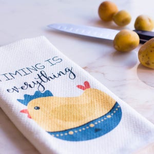 May include: White kitchen towel with a yellow chick illustration and the text "TIMING IS everything".