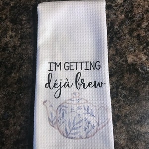May include: White kitchen towel with a blue and white teapot design and the text "I'm getting d&eacute;j&agrave; brew".