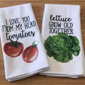 K&ouml;nnte beinhalten: Zwei wei&szlig;e K&uuml;chent&uuml;cher mit einem gr&uuml;nen Salat und roten Tomaten darauf gedruckt. Die Handt&uuml;cher haben den Text "I love you from my head tomatoes" und "lettuce grow old together" darauf gedruckt.