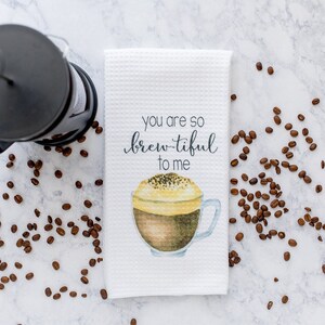 May include: White kitchen towel with a watercolor illustration of a cup of coffee and the text "You are so brew-tiful to me".