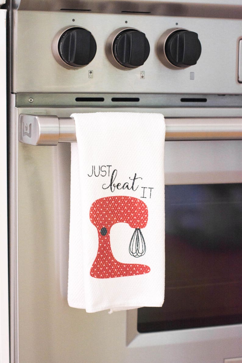 May include: White kitchen towel with a red and white polka dot stand mixer illustration and the text "Just beat it".