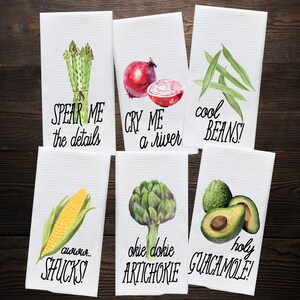 K&ouml;nnte beinhalten: Sechs wei&szlig;e K&uuml;chent&uuml;cher mit Aquarell-Illustrationen von Gem&uuml;se und Wortspielen. Die Handt&uuml;cher zeigen Spargel, Zwiebeln, gr&uuml;ne Bohnen, Mais, Artischocken und Avocados. Der Text auf den Handt&uuml;chern lautet: "Spear Me the details", "Cry Me a River", "Cool Beans", "Aw, Shucks", "Okie Dokie Artichoke", und "Holy Guacamole!"