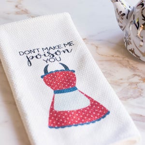 May include: White kitchen towel with red and blue polka dot apron design and the text "Don't make me poison you".