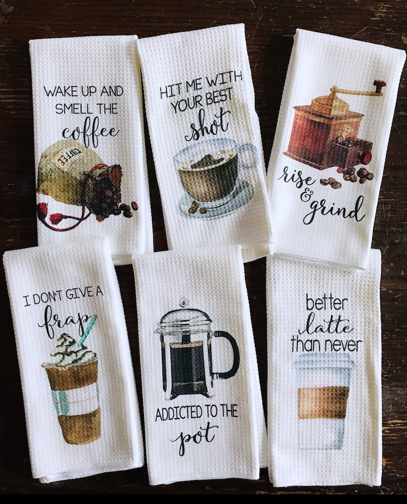 May include: Set of six white kitchen towels with coffee-themed designs and sayings. The towels feature illustrations of coffee beans, coffee cups, a coffee grinder, and a French press. The sayings on the towels include "Wake up and smell the coffee", "Hit me with your best shot", "Rise and grind", "I don't give a frap", "Addicted to the pot", and "Better latte than never".