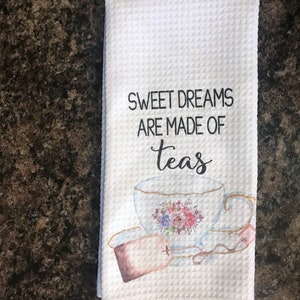 May include: White tea towel with a watercolor illustration of a teacup and tea bag. The text "Sweet Dreams Are Made Of Teas" is printed in black.