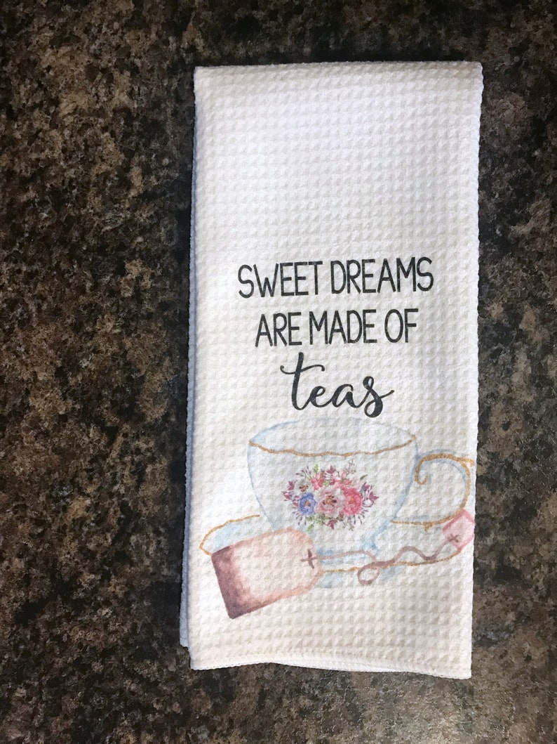 May include: White tea towel with a watercolor illustration of a teacup and tea bag. The text "Sweet Dreams Are Made Of Teas" is printed in black.