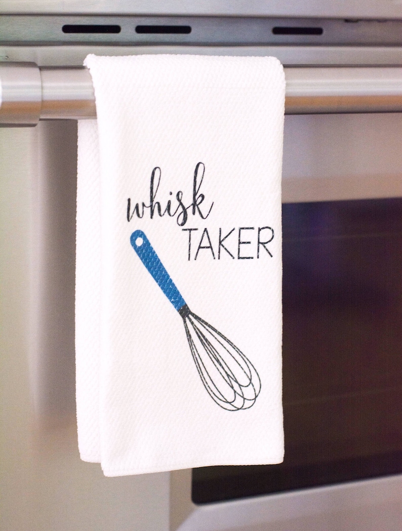 May include: White kitchen towel with a blue and black whisk illustration and the text "whisk taker" in black.