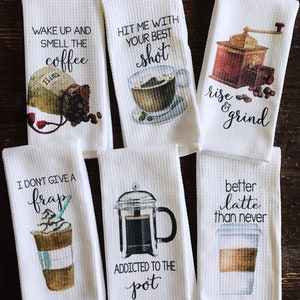 May include: Set of six white kitchen towels with coffee-themed designs and sayings. The towels feature illustrations of coffee beans, coffee cups, a coffee grinder, and a French press. The sayings on the towels include "Wake up and smell the coffee", "Hit me with your best shot", "Rise and grind", "I don't give a frap", "Addicted to the pot", and "Better latte than never".