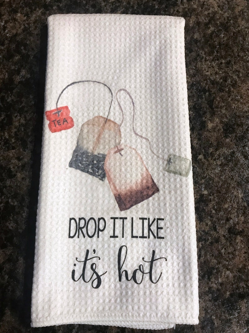 May include: White tea towel with a brown and black tea bag illustration and the text "DROP IT LIKE IT'S HOT".
