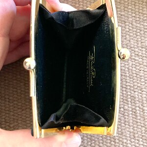 May include: A gold-toned metal coin purse with a black velvet interior. The purse is open and the interior is visible. The purse has the text "Furla" and "Made in Italy" printed on the inside.
