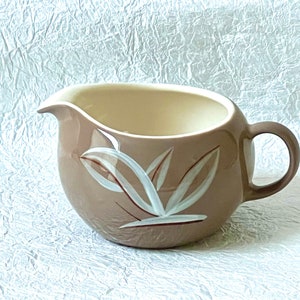 May include: A brown ceramic creamer with a white leaf design. The creamer has a rounded body and a handle.