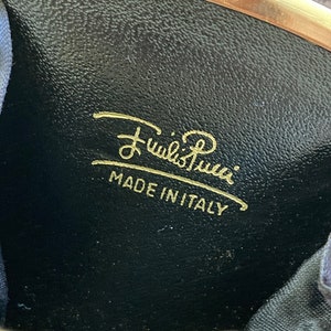 May include: A black leather coin purse with gold-toned hardware and the inscription "Furla's Roma" in gold lettering. The purse also has the text "Made in Italy" in gold lettering.